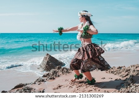 Hawaiian woman enjoys hula dancing on the beach barefoot wearing traditional costume. Tropical lady at beach with flower crown on her head and neck. Ready to party. Summer landscape in a sunny day.
