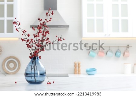 Hawthorn branches with red berries on table in kitchen, space for text