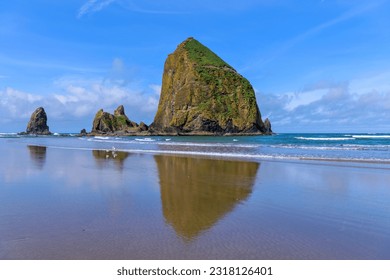 Haystack Rock - A sunny Spring morning view of famous Haystack Rock reflecting on smooth sandy Cannon Beach. Oregon, USA.