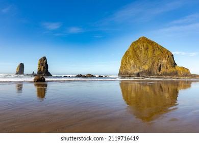 Haystack rock wide angle view with  reflective water at coastline edge on blue sky sunny afternoon.