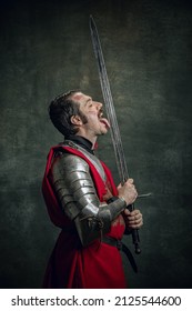 Hazard. Comic Portrait Of Funny Medieval Warrior Or Knight With Dirty Wounded Face Holding Sword Isolated Over Dark Background. Comparison Of Eras, History, Renaissance Style. Art, Meme