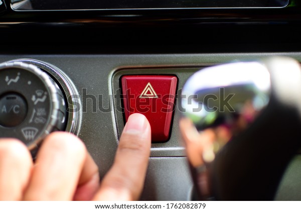 Hazard signal button for asian car with\
finger press on it. Selective focus\
image