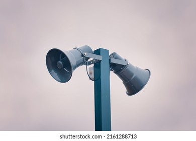 Hazard warning system. Tall metal column with two gray loudspeakers against cloudy sky. Providing security in the city, notification of emergencies. Copy space for text.