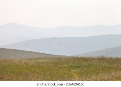 Haze and smoke from forest fires over the hills and steppe on hot summer day. Shore of Baikal Lake, steppe part of Olkhon Island. Natural disaster. Beautiful landscape with hills in sfumato