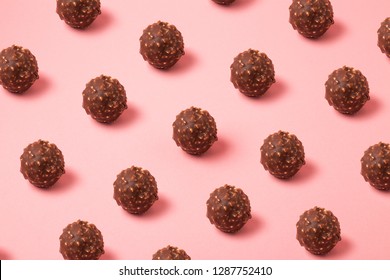 Hazelnut chocolate balls pattern on pink background, chocolate pralines backdrop
