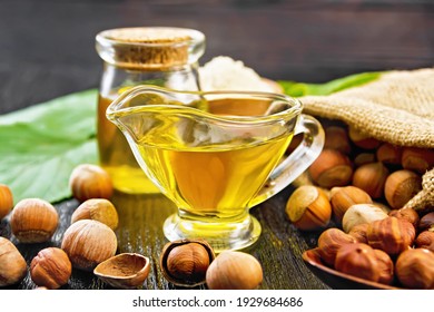 Hazelnut Oil In A Glass Jar And Gravy Boat, Flour In A Bowl, Nuts In A Bag, Spoon And On The Table, Filbert Sprigs With Green Leaves On Dark Wooden Board Background