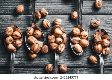 Hazelnuts background. Nuts on spoons. Five silver spoons on gray wood. Wooden table nuts background. Rustic colors healthy snack. Food on wood. Shelled hazlenuts texture. Foto Stok