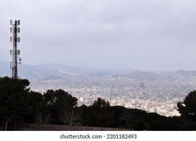 Hazy City Skyline View With Trees And Telecom Mast In Foreground