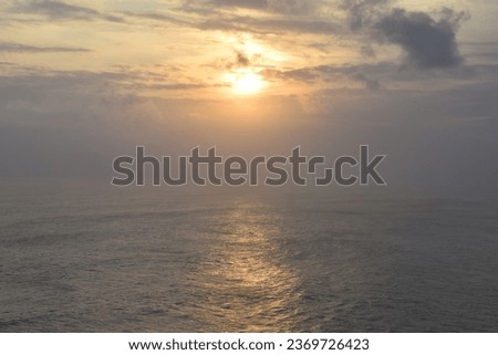 A hazy orange evening sunset in Bali, Indonesia.  Looking out over the Pacific Ocean.  A few clouds in the sky.  Sun reflected on the water.  May 2018.