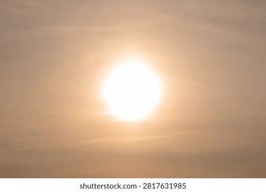 A Hazy Sun Glows Through Thin Clouds as the Evening Sky Softens Over the Czech Countryside - A bright sun shines through a veil of thin atmospheric clouds, filling the sky with warm golden and amber tones. The diffused light softens the scene and creates a gentle gradient across the sky, reducing contrast and producing an almost ethereal appearance. Minimalist in composition, the photograph focuses on the interaction between sunlight and cloud cover, highlighting subtle variations in color and atmosphere. The image captures a quiet moment near the end of the day when filtered sunlight transforms the sky into a luminous natural backdrop and conveys a sense of warmth, calm, and seasonal change.