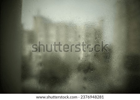 Hazy and surreal view of residential building through a window during rainy season. Water droplet formed on window due to air condensation.