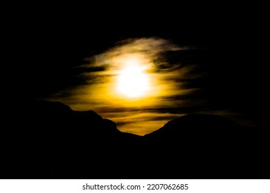 Hazy, Yellow Sun In Dark Sky Over Silhouetted Mountainside