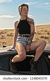 HDR Portrait Of A Woman In Shorts Sitting On The Roof Of A Car, Against The Background Of The Desert