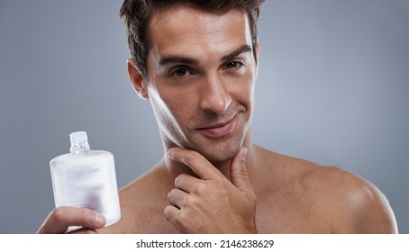 He always looks and smells great. Studio shot of a handsome young man applying aftershave to his face.