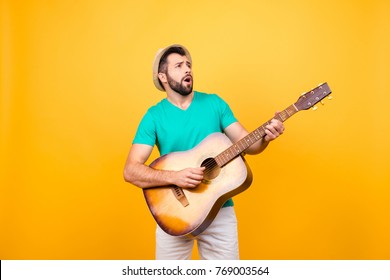 He is finding notes for the new popular song! Cheerful joyful excited musician playing the acoustic guitar, isolated on yellow background