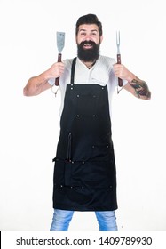 He is a great cook. Happy grill cook with cooking utensils. Bearded man holding fork and spatula for cooking and serving barbecue. Master cook wearing grilling apron. Chief cook in workwear. Cookout.