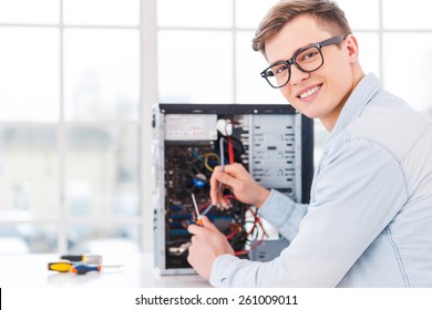 He loves his job. Portrait of handsome young man repairing computer while sitting at his working place