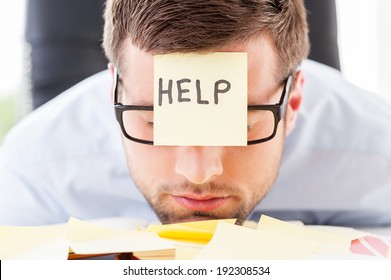 He needs help. Frustrated young man in formal wear with adhesive note on his forehead leaning his head at the table - Powered by Shutterstock