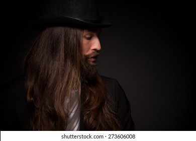 He Is A Rock Star And He Can Play Guitar. Hipster With Long Hair And Beard, Weared In Topper And Black Suit On Dark Background