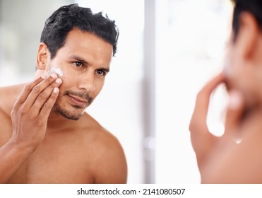 He takes great care of his skin. A young man applying cream to his face while looking in the mirror. - Powered by Shutterstock