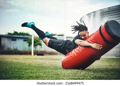 He trains like the rugby pro he is. Full length shot of a handsome young rugby player working out with a tackle bag on the playing field. - Powered by Shutterstock