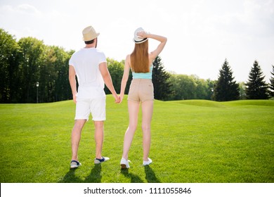 He vs She together forever! Rear view fullbody portrait of attractive lovely couple in shorts sneakers straw hats holding hands walking outside enjoying beauty of landscape trees