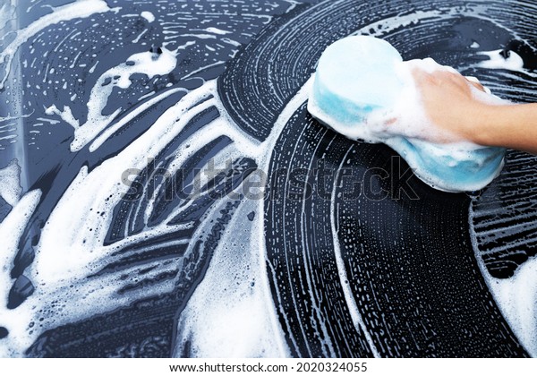 He was washing his car with a blue sponge and foam\
for washing the car.