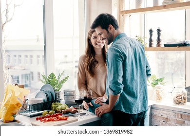 He Will Never Let Her Go. Beautiful Young Couple Cooking Dinner And Drinking Wine While Standing In The Kitchen At Home