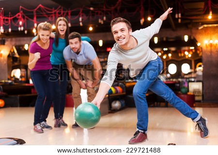 He is a winner. Handsome young men throwing a bowling ball while three people cheering  