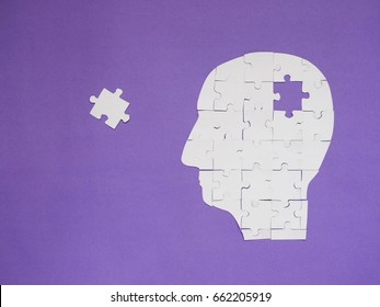Head brain white puzzle with missing pieces from jigsaw puzzle on purple background. Creative idea for memory loss, dementia, Alzheimer's disease and mental health concept. Copy space.