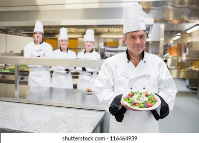 Head chef presenting salad with his team standing behind him - Powered by Shutterstock