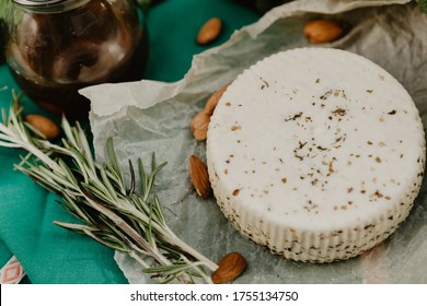 A Head Of Goat's Milk Cheese With Spices With A Jar Of Honey, Almond Nuts And A Sprig Of Rosemary On A Green Background.