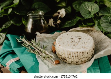 A Head Of Goat's Milk Cheese With Spices With A Jar Of Honey, Almond Nuts And A Sprig Of Rosemary On A Green Background.