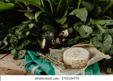 A Head Of Goat's Milk Cheese With Spices With A Jar Of Honey, Almond Nuts And A Sprig Of Rosemary On A Green Background.