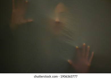 Head and handprint of woman as she suffocates behind fabric, raised hands and wide open mouth. Mystery concept. Shadow blur of screaming woman. Touching the void. Close up photo. 
