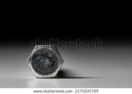 The head of a hexagonal metal bolt on a gray black background. Stainless steel bolt for screwing, fastening, fixing. Metal construction anchor for hardware store and furnitures.