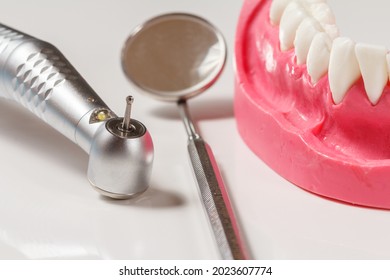 Head of high-speed dental handpiece with bur, a metal mirror and a layout of the human jaw on the white background. Dental instruments for dental treatment. Close-up view.