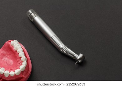 Head of high-speed dental handpiece with bur and a layout of the human jaw on the black background. Dental instruments for dental treatment. Top view.