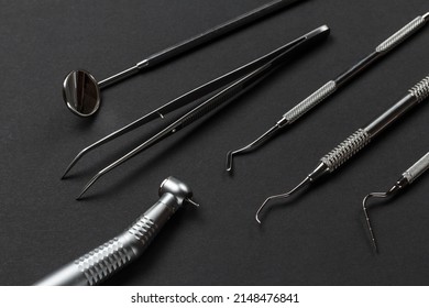 Head of high-speed dental handpiece, a mouth mirror, tweezers, a dental restoration instrument, a curette and a plugger on the black background. Medical tools.