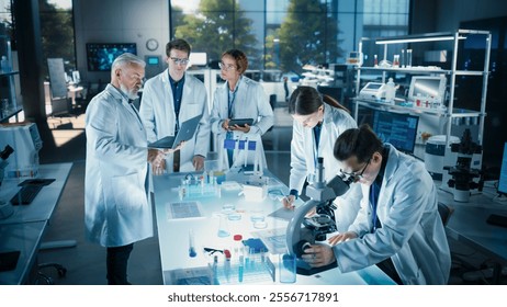 Head of Laboratory Making a Bioengineering Experiment with a Group of Young Science College Students. Future Specialists Working with Modern Microscopes, Using Tablet and Laptop Computers