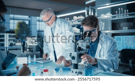 Head of Laboratory Making a Bioengineering Experiment with a Group of Young Science College Students. Future Specialists Working with Modern Microscopes, Using Tablet and Laptop Computers