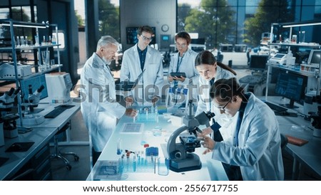 Head of Laboratory Making a Bioengineering Experiment with a Group of Young Science College Students. Future Specialists Working with Modern Microscopes, Using Tablet and Laptop Computers