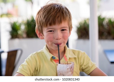 Head Portrait Of Lovely And Sweet Young Kid 7 Or 8 Years Old In Yellow Shirt  Enjoying Happy Drinking Ice Cream Smoothie Milk Shake With Straw In Childhood And Lifestyle Concept