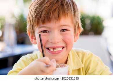 Head Portrait Of Lovely And Sweet Young Kid 7 Or 8 Years Old In Yellow Shirt  Enjoying Happy Drinking Ice Cream Smoothie Milk Shake With Spoon In Childhood And Lifestyle Concept