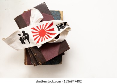 Head Scarf Of A Japanese Kamikaze Pilot Of World War II. Below Are Some Old Books. The English Translation Of The Words That Are Written On The Handkerchief Is, Divine Wind