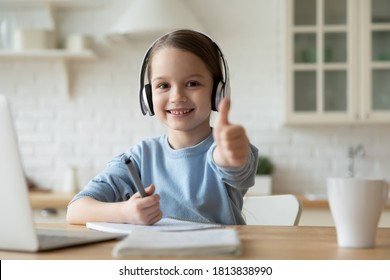 Head shot adorable little european kid girl wearing wireless headphones, sitting in front of computer, enjoying online education courses at home, showing thumbs up gesture, e-learning concept. - Powered by Shutterstock