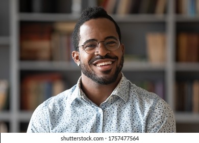 Head shot of african american bearded guy with pierced ear casual shirt smiling looking at camera standing indoor. Webcam view, conference video call, confident company representative portrait concept