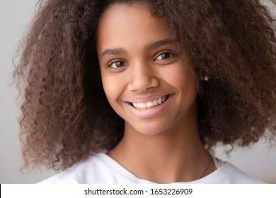 Head shot of african american teen girl looking at camera, black female adolescent teenager with pretty face posing alone, smiling teenage generation z school child with afro hair close up portrait