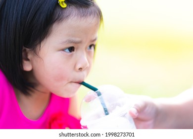 Head Shot Of Asian Kid Girl Sucking Sweet Coconut Smoothie. Mom Holding Glass To Feeding Daughter. Baby Drinking Cool Water With Tube. Summer Time, Hot Day. Copy Space. Children Aged 4-5 Years Old.