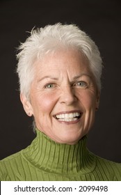 Head Shot Of A Beautiful 55 To 60 Year Old Woman Against A Black Background.